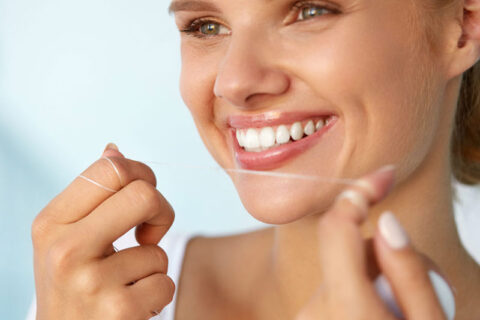 a person smiling and flossing her teeth