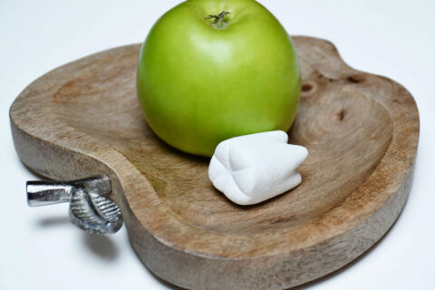 a green apple and a white tooth on a wooden plate
